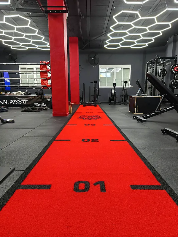 Pista roja de arrastre de trineo para Hyrox con marcas de distancia, columnas rojas y el ring al fondo